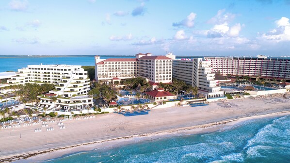 A beachfront hotel with multiple buildings, a swimming pool, and beach umbrellas.