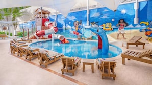 An indoor pool area with slides, lounge chairs, and a mural depicting ocean scenes.