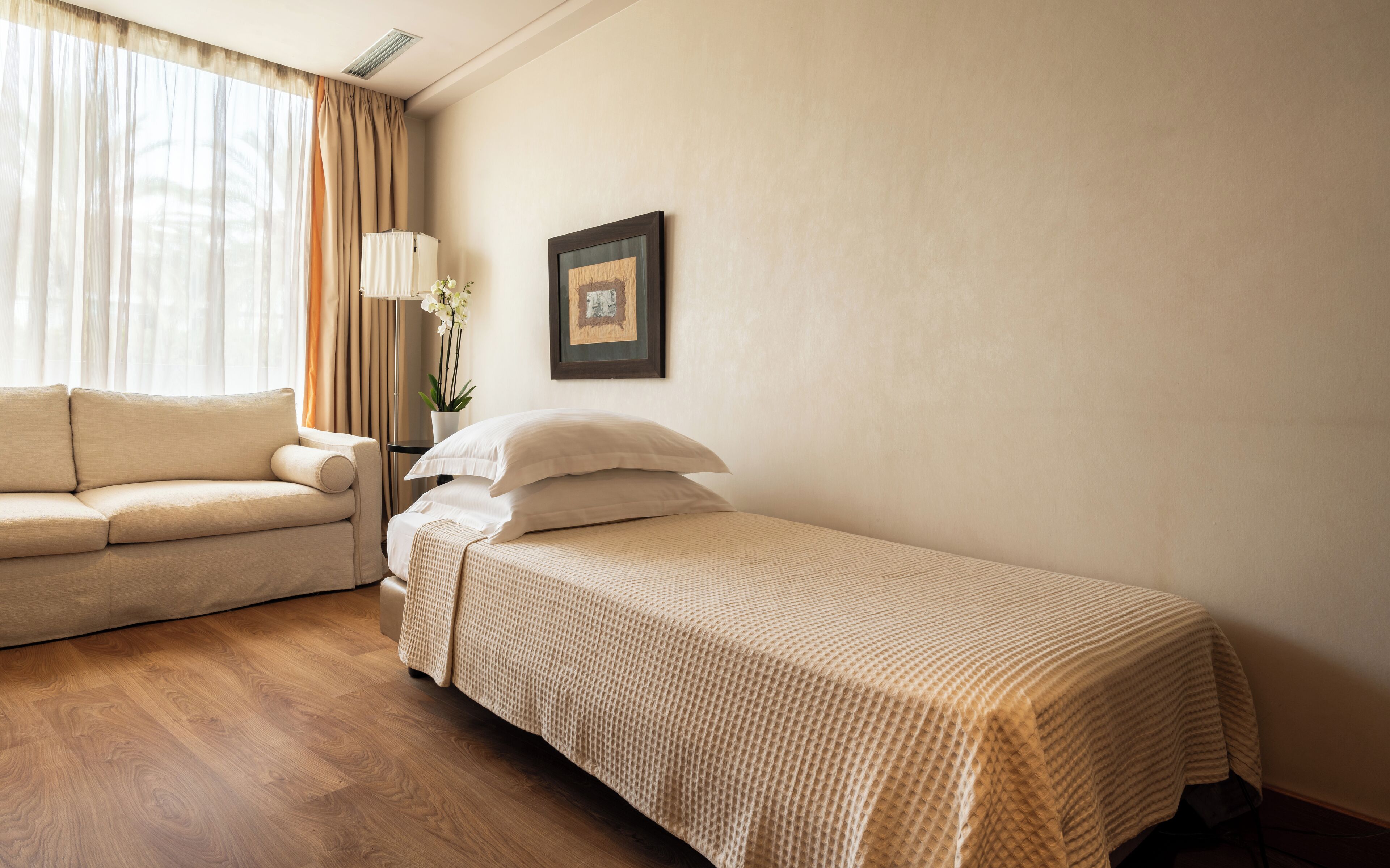 Habitación de hotel con cama, sofá, lámpara y un cuadro en la pared.