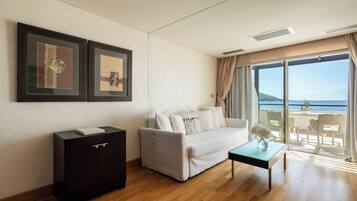 Una sala de estar moderna con un sofá blanco, un aparador de madera oscura y una mesa de centro de vidrio. Hay dos cuadros en la pared y un ventanal con vistas al mar.