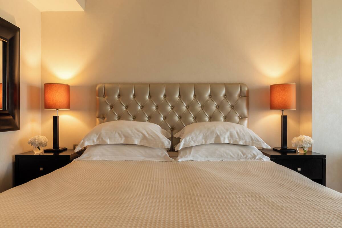 A neatly made bed with a tufted headboard, two bedside tables with lamps, and a vase with flowers on each side.