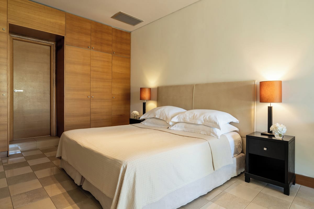 A hotel room with a large bed, wooden wardrobe, two bedside tables with lamps, and a small vase with flowers.