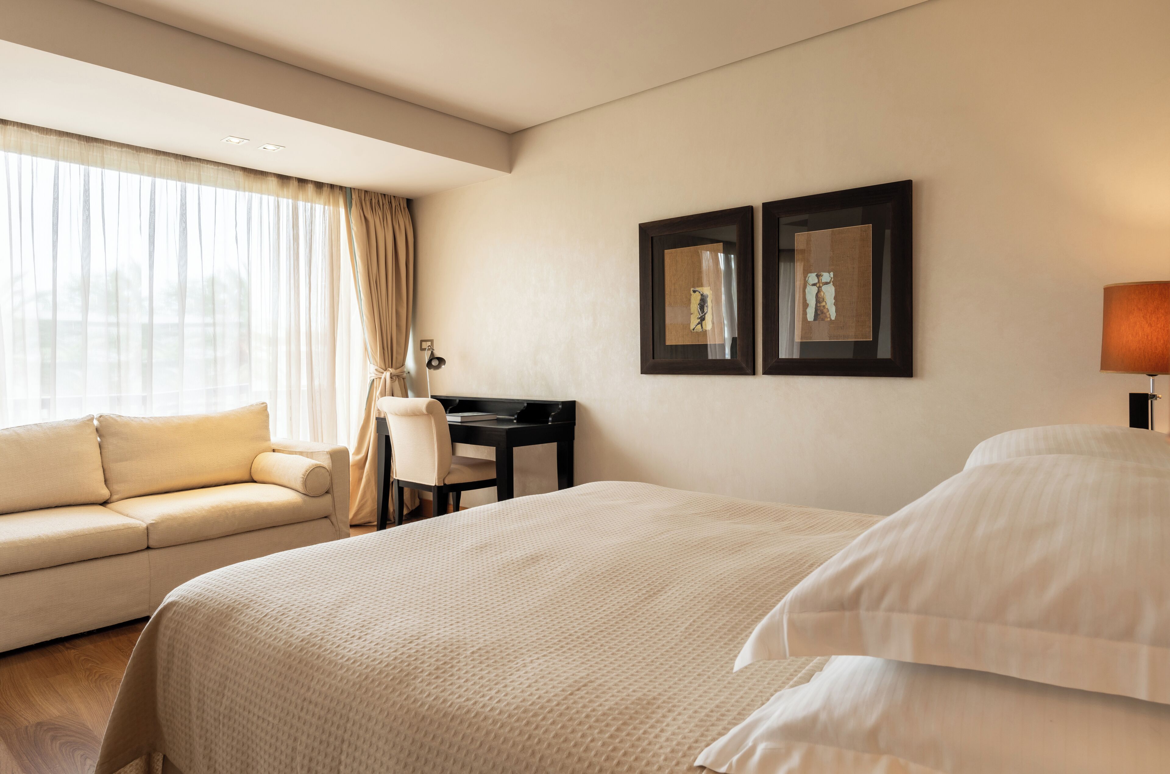 Habitación de hotel con una cama grande, un sofá, un escritorio y dos cuadros en la pared.