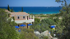 A coastal building with a balcony overlooking the sea, surrounded by greenery and blue umbrellas. - Stelle Marine (Arzachena)