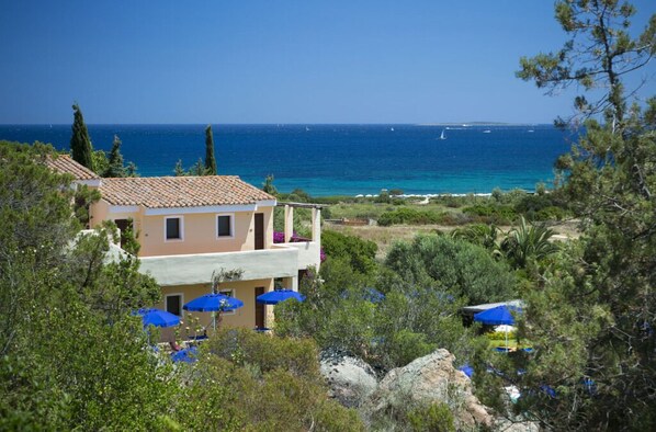 A coastal building with a balcony overlooking the sea, surrounded by greenery and blue umbrellas. - Stelle Marine (Arzachena)