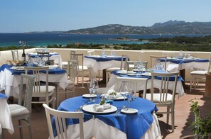 An outdoor dining area with tables set for a meal, overlooking a scenic coastal view. - Stelle Marine (Arzachena)