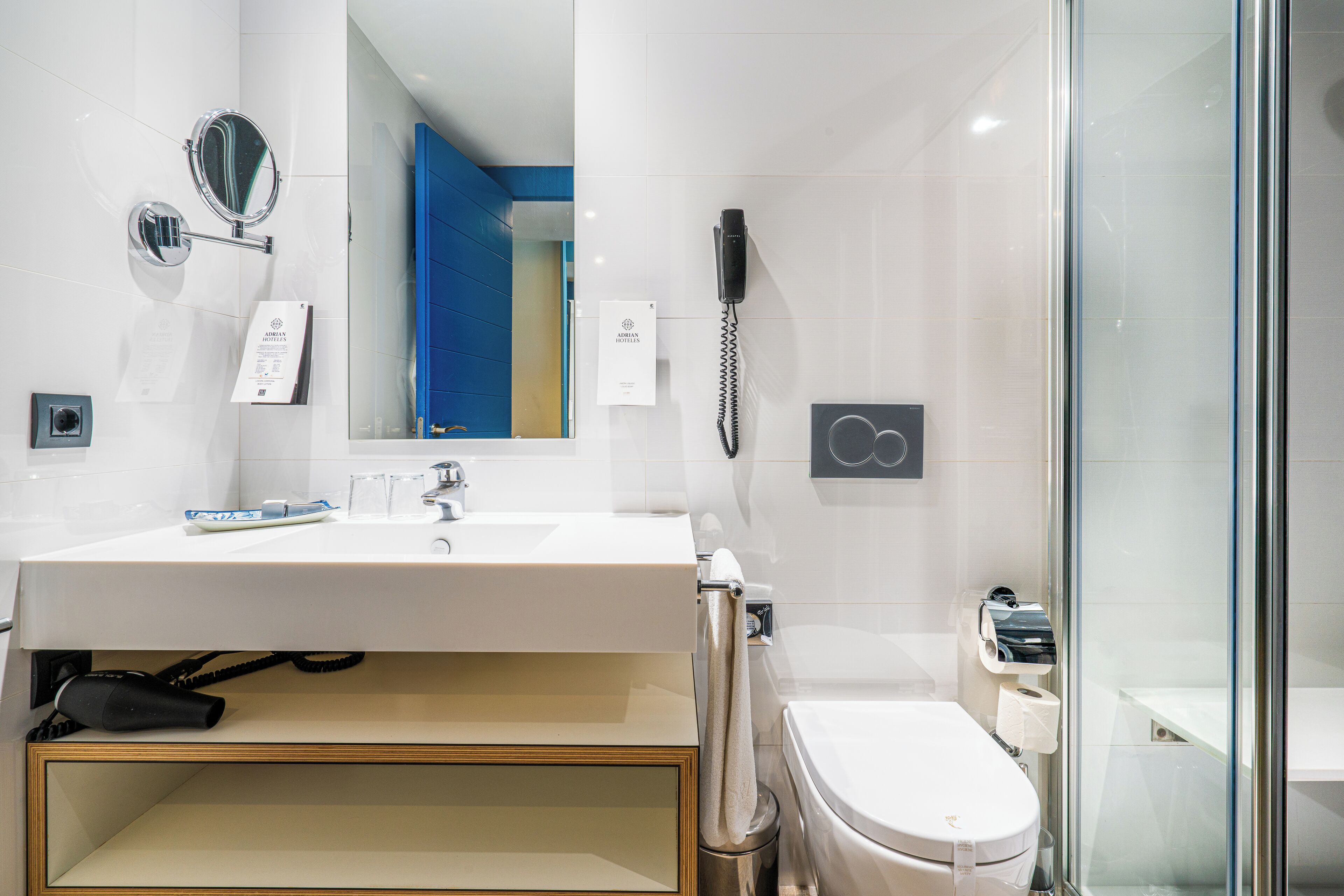 A modern bathroom with a large sink, a mirror, a hairdryer, a telephone, and a toilet.
