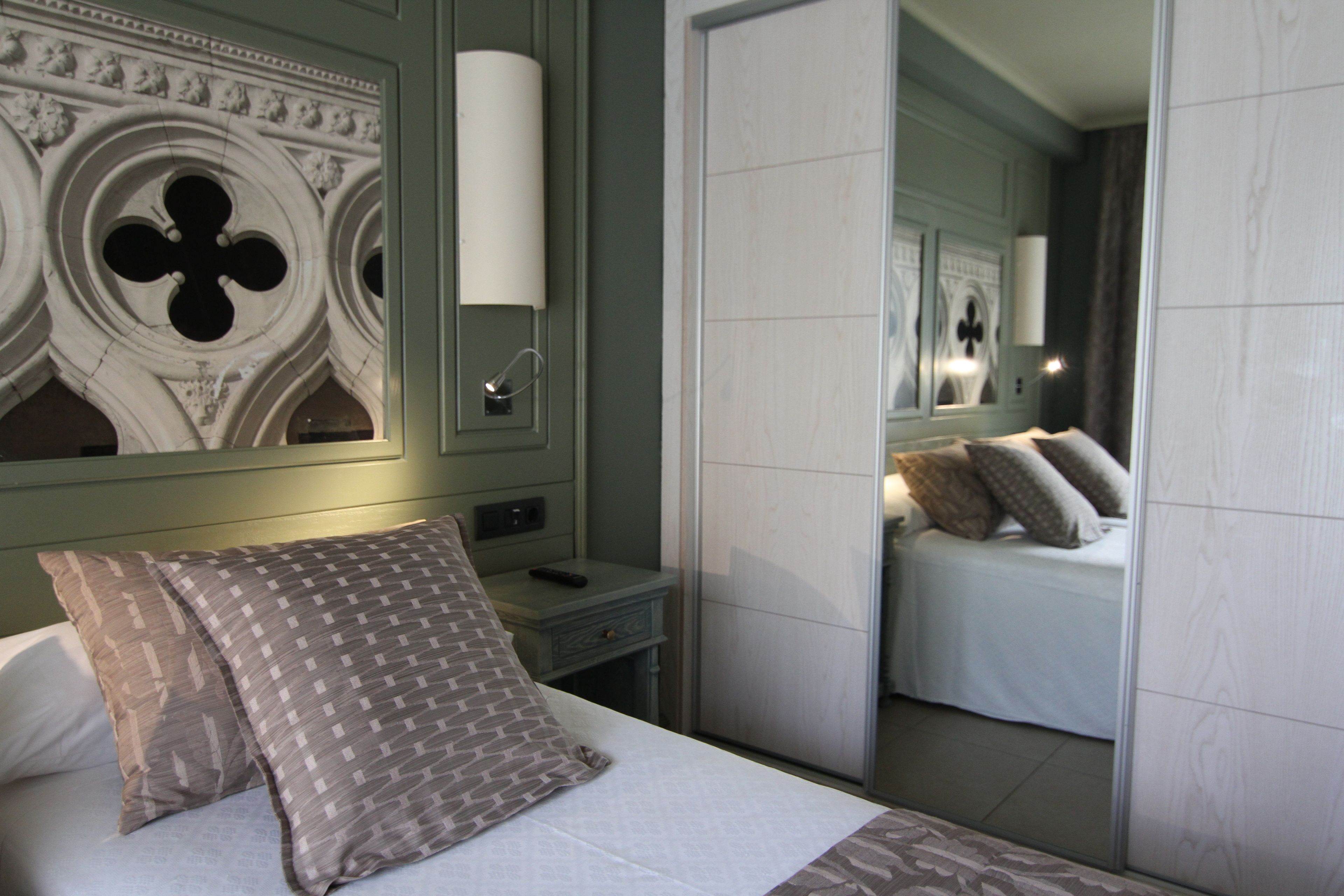 A bedroom with a bed, a nightstand, a mirror, and a wall with decorative molding.