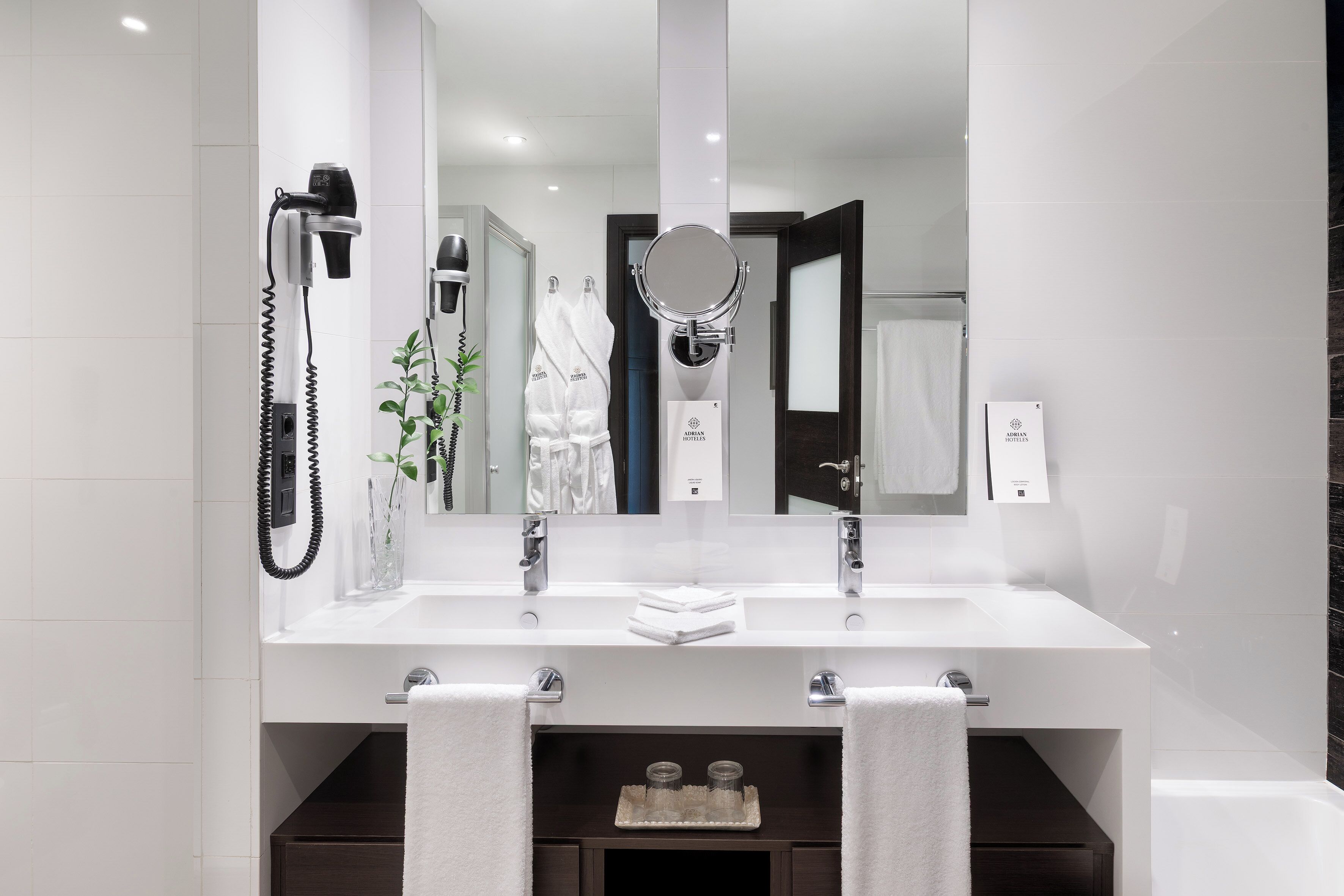 A modern bathroom with a large mirror, two towel racks, a hairdryer, and a plant.