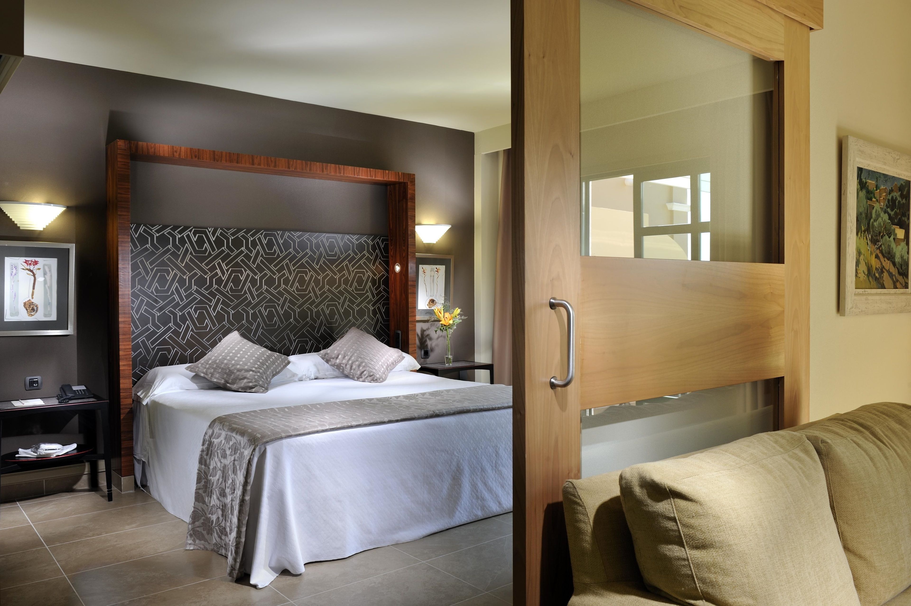 Habitación de hotel con una cama grande, cabecera de madera, mesita de noche, escritorio y sofá.
