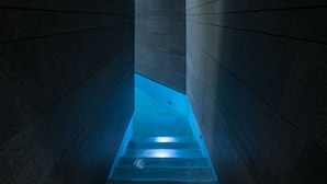 Un escalier étroit dont l’intérieur est éclairé d’une lumière bleue, entouré de murs sombres.