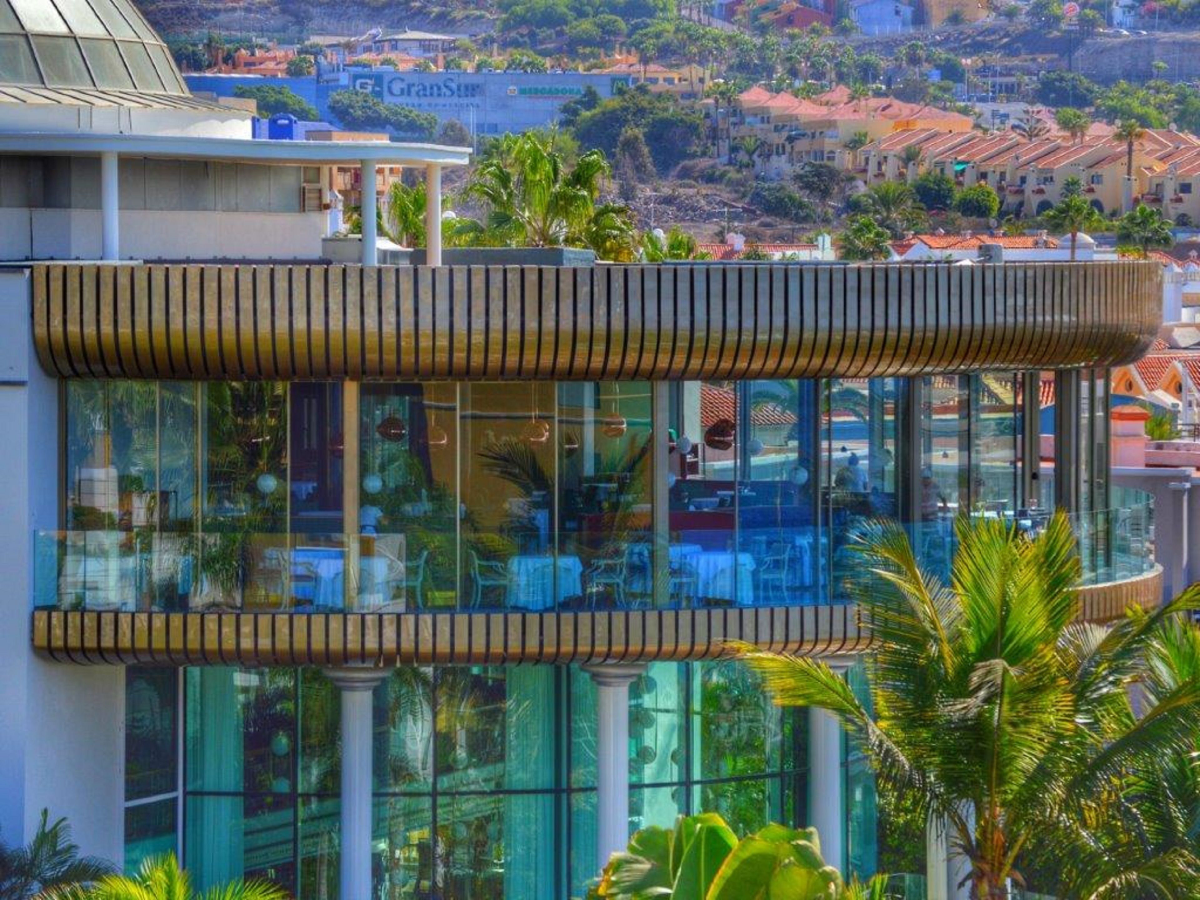 A modern hotel with a glass facade, outdoor seating, and a view of the surrounding cityscape.