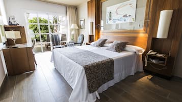 A hotel room with a large bed, a desk with a lamp, a chair, a telephone, and a window with curtains.