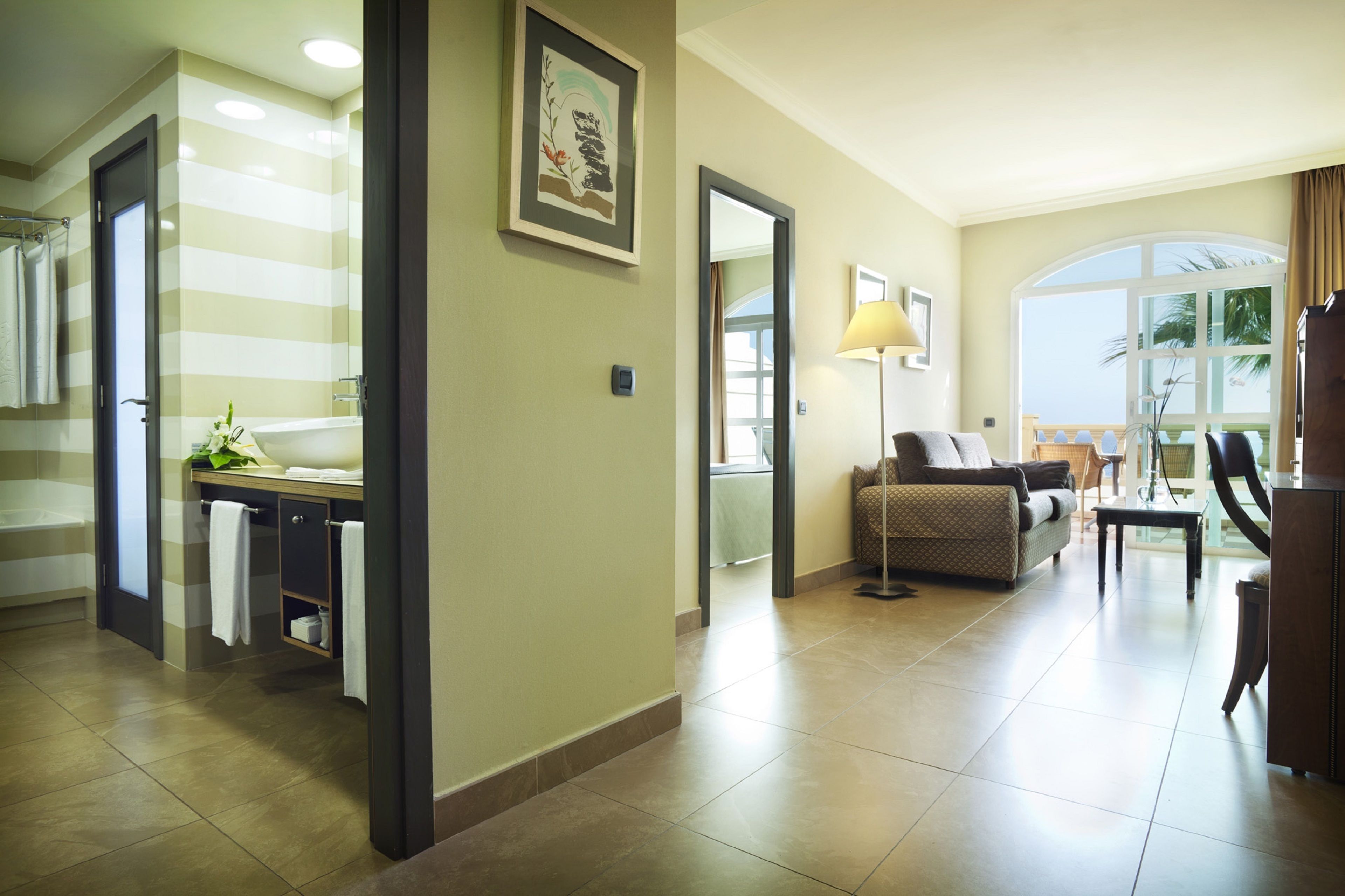 Habitación de hotel con baño, zona de estar con sofá y mesa, y balcón con vistas.