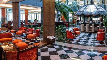 Eine Lobby mit Schachbrettfußboden, roten und schwarzen Sesseln, einem Barbereich und einer großen, glasverglasten Kuppel.