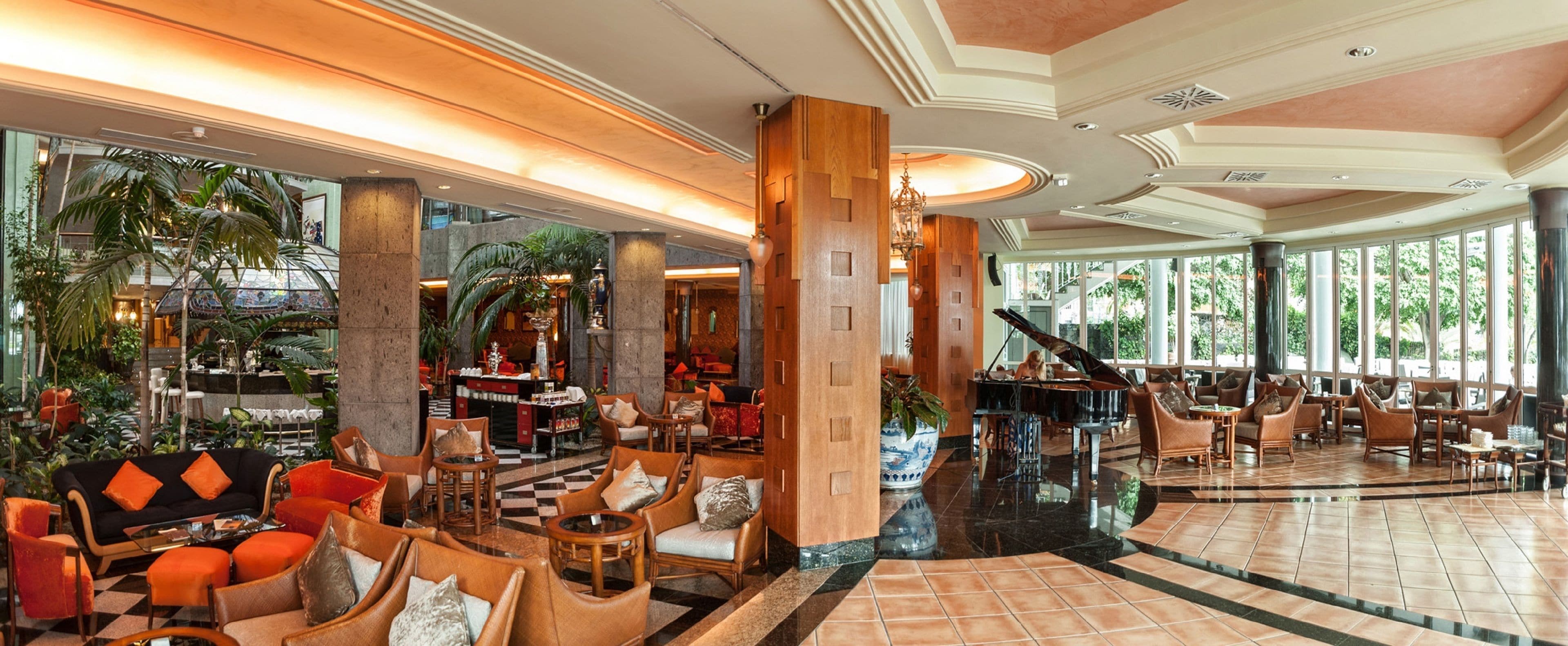 A spacious lobby with a grand piano, comfortable seating areas, and a large indoor garden.