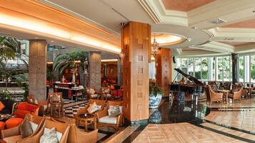 A spacious lobby with a grand piano, comfortable seating areas, and a large indoor garden.