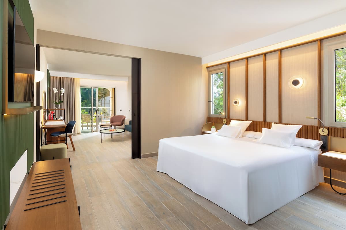 Ein modernes Hotelzimmer mit einem großen Bett, einem Schreibtisch und einer Sitzecke mit Blick ins Freie.