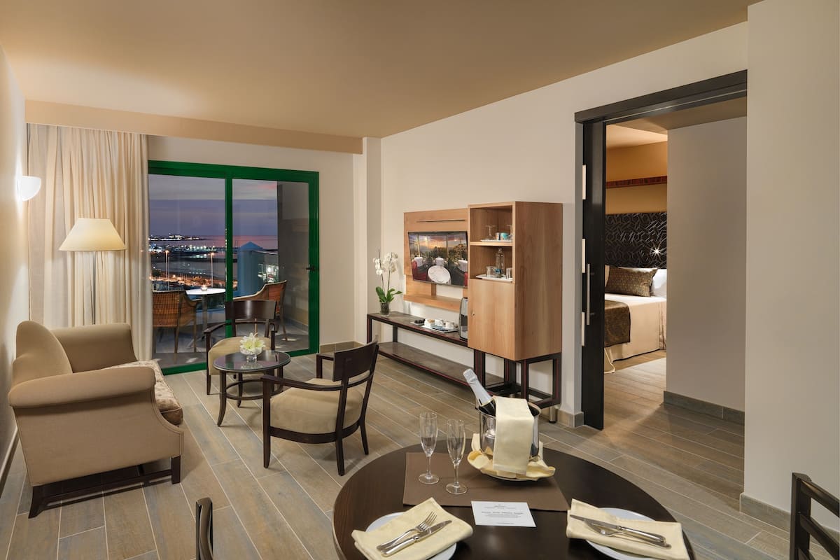 Ein Hotelzimmer mit Essbereich, einer Couch, einem Tisch für zwei Personen und Blick auf die Stadt durch große Fenster.