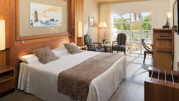 Habitación de hotel con una cama grande, un escritorio, una silla y una ventana con vistas a palmeras.