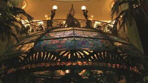 Un vaste atrium surmonté d’une grande coupole en vitrail, agrémenté de balustrades décoratives et doté d’un escalier central.