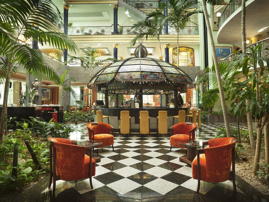 Un hall d’entrée avec un sol à carreaux, un bar central et des plantes tropicales.