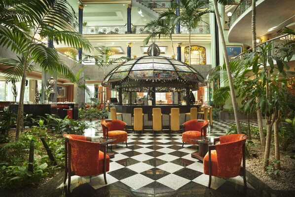 Un vestíbulo con piso a cuadros, una zona de bar central y plantas tropicales.