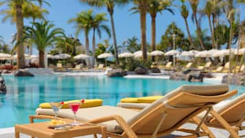 Un área junto a la piscina con sillones de mimbre, una mesa con una bebida y sombrillas.
