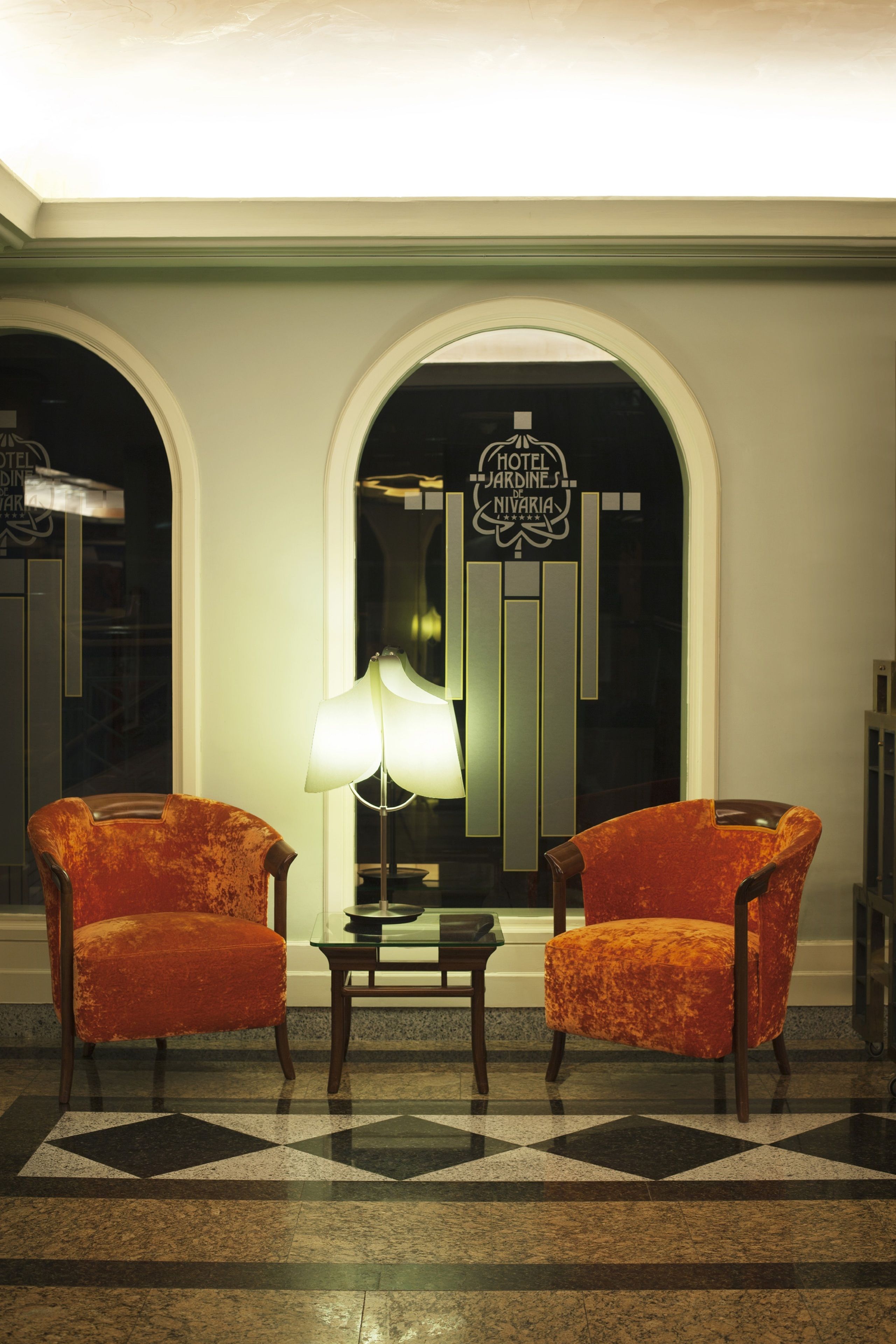A lobby with two orange armchairs, a table, and a lamp.