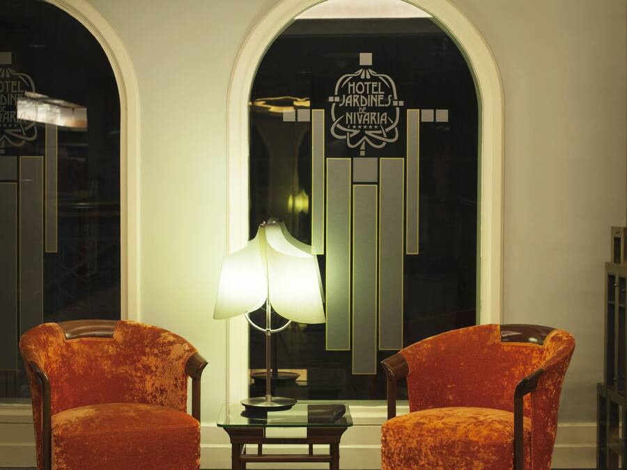 A lobby with two orange armchairs, a table, and a lamp.