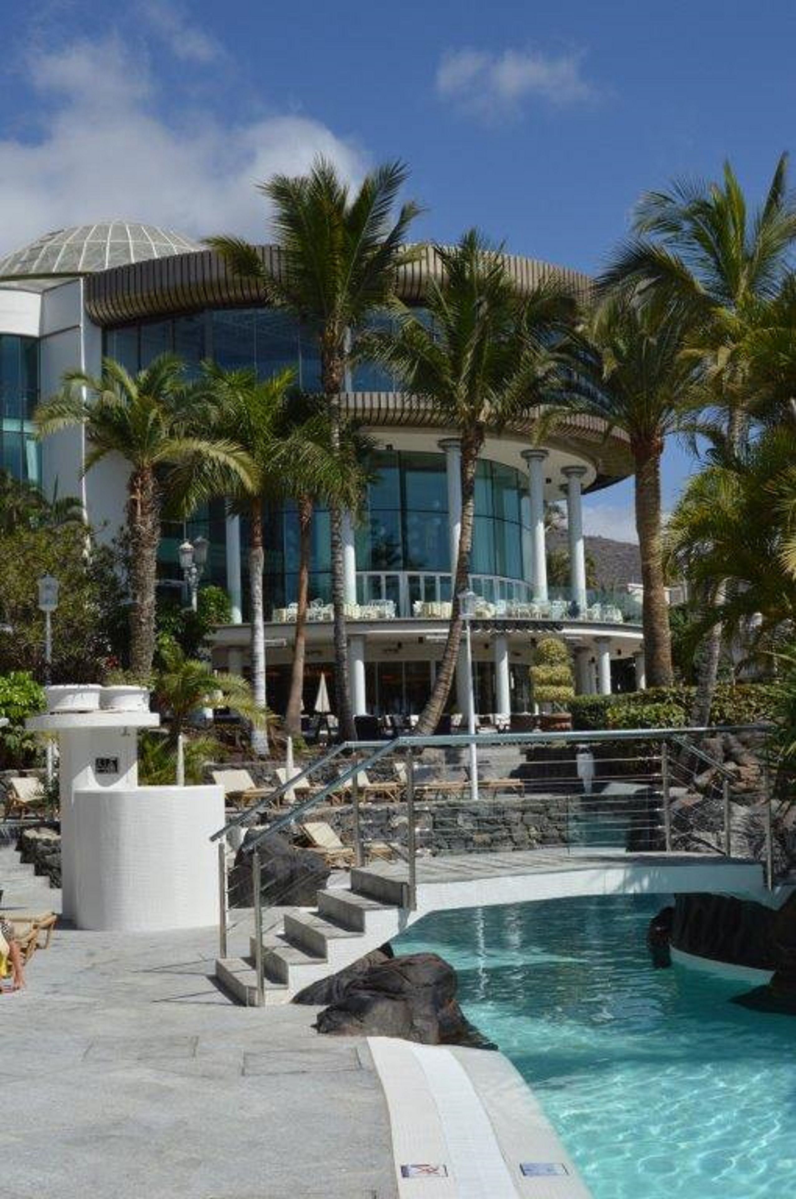 A resort with a pool, palm trees, and a modern building with large windows.