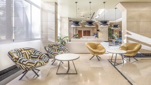 Een moderne lobby met een bank, twee fauteuils met een patroon, een ronde tafel en hanglampen.
