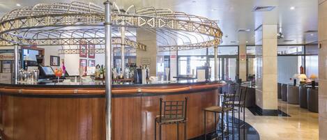 A modern bar area with a curved wooden counter, metal chairs, and a decorative ceiling structure.