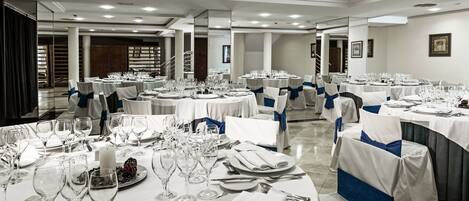 A banquet hall with round tables set for dining, each with white tablecloths and blue sashes.