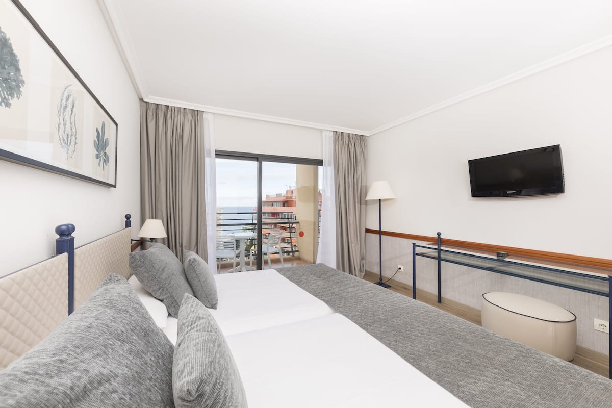 Une chambre d’hôtel avec un lit, une télévision, un balcon avec vue et un bureau avec une lampe.