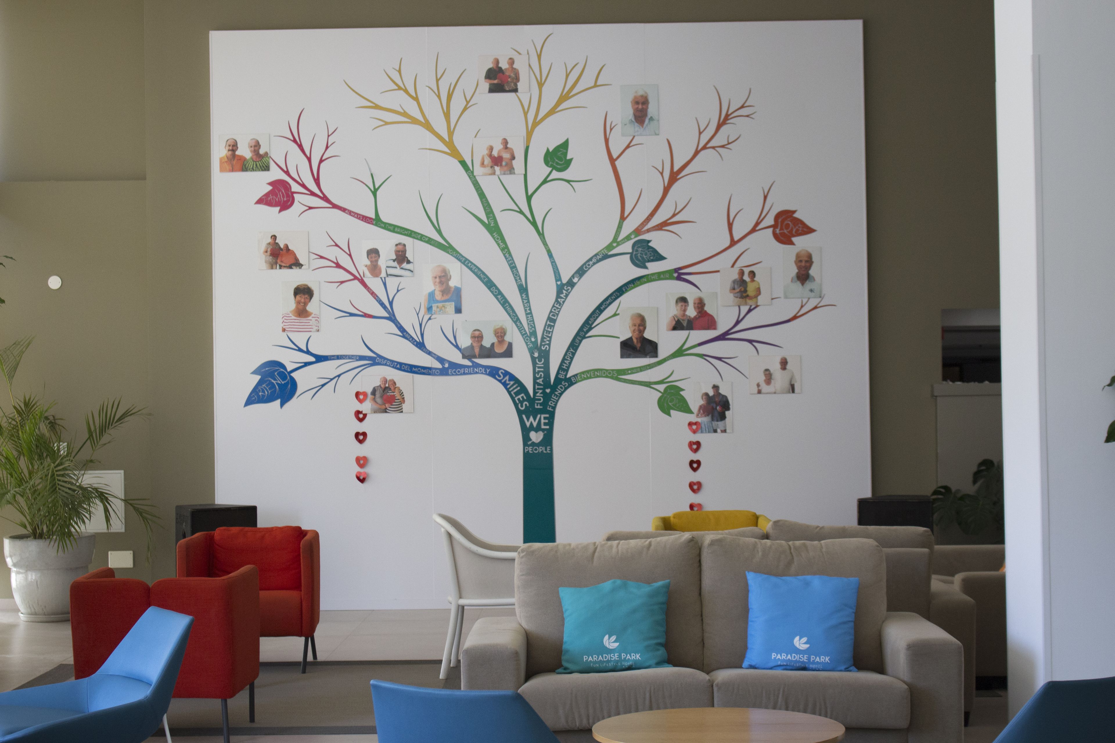Un hall d’entrée orné d’une grande fresque représentant un arbre généalogique, avec un espace détente comprenant des fauteuils et des canapés, ainsi qu’une plante en pot.