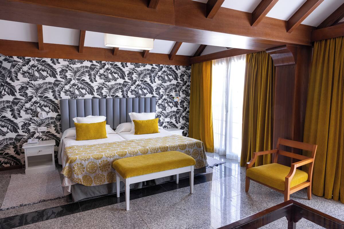 Una habitación de hotel con una cama, una mesita de noche, un banco y una silla.
