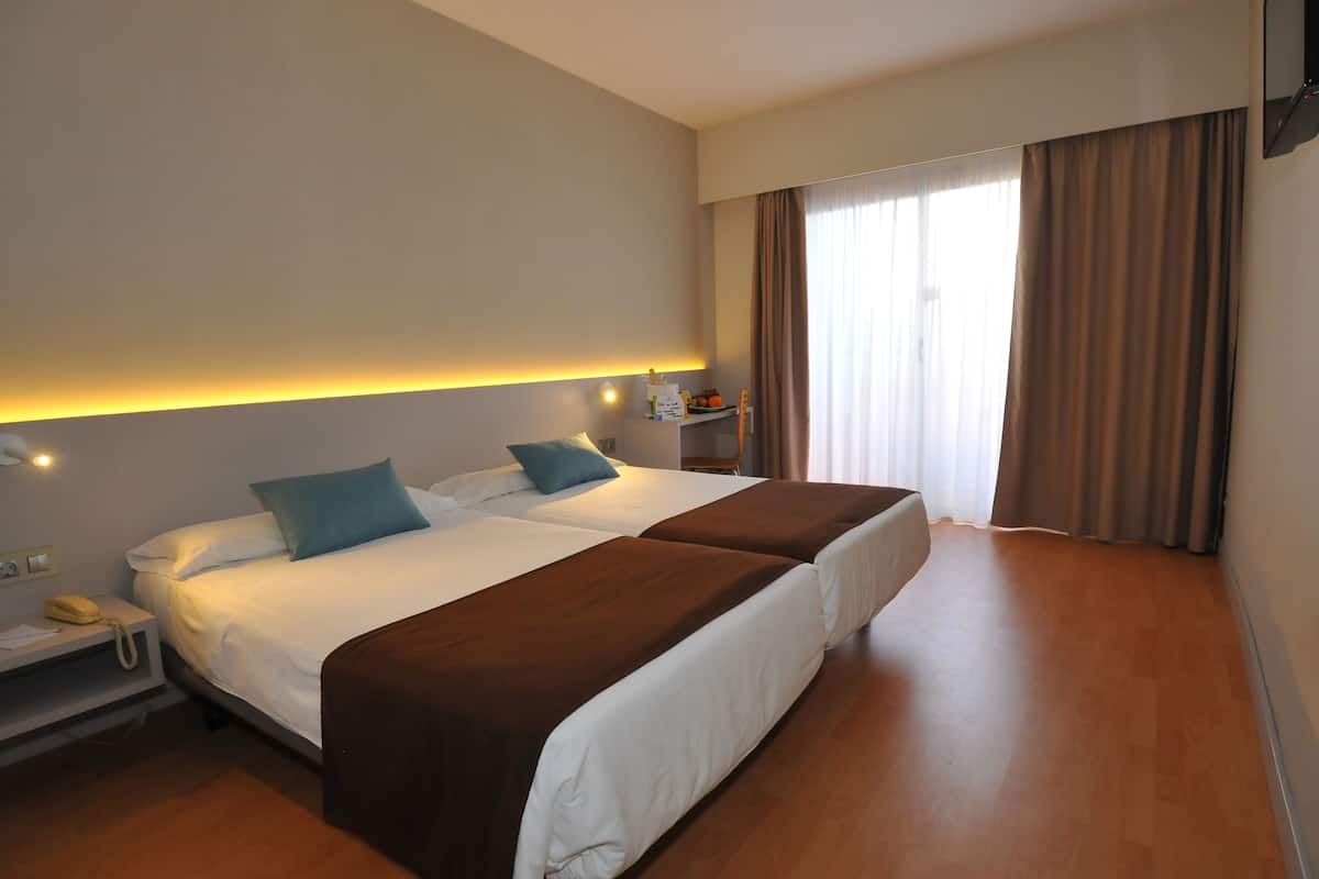 Habitación de hotel con dos camas, una mesita de noche con teléfono y una ventana con cortinas.