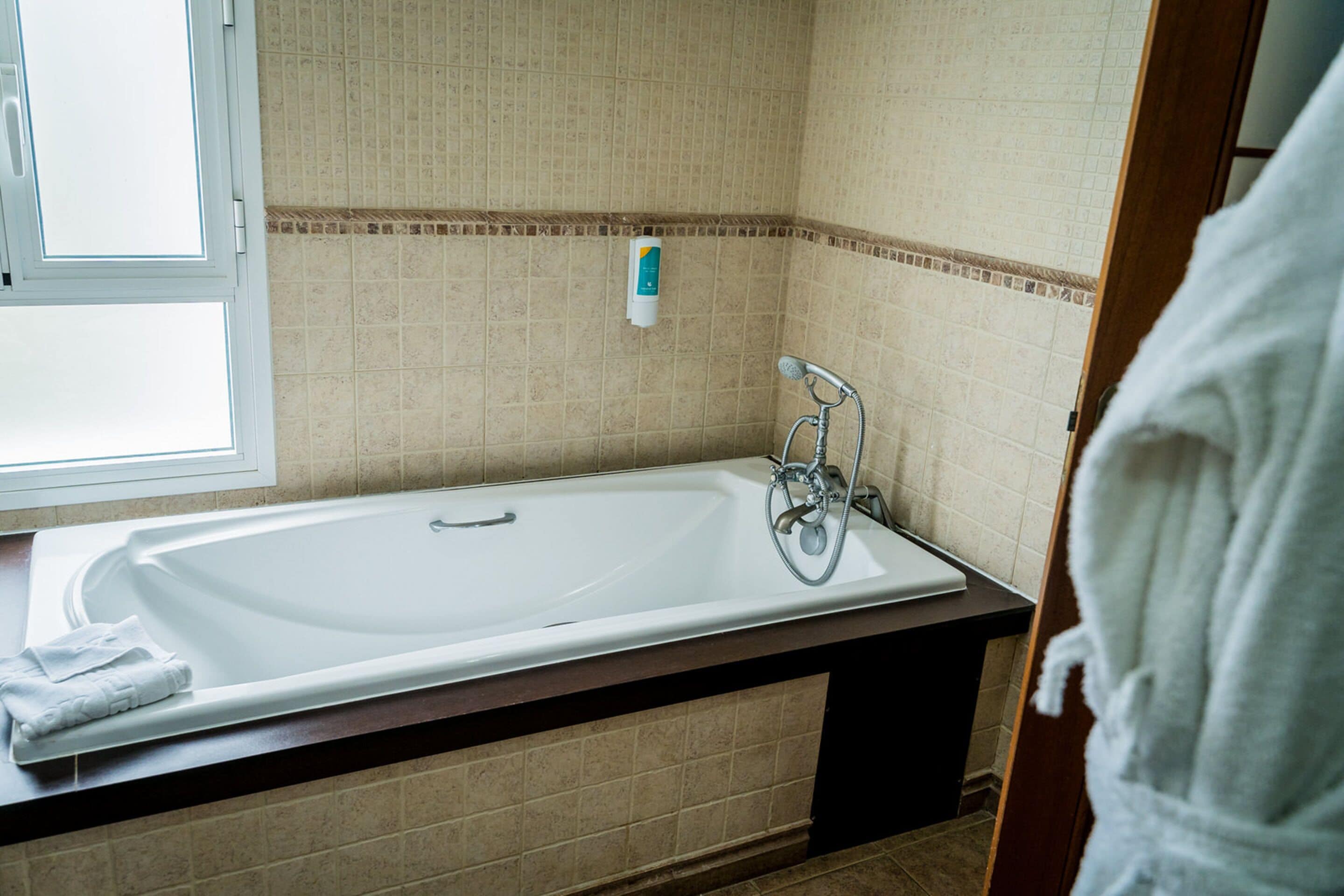 A bathroom with a bathtub, a towel, and a window.