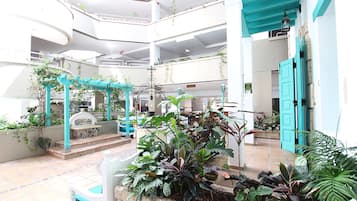 Ein mehrgeschossiges Atrium mit einem zentralen Gartenbereich, verschiedenen Sitzgelegenheiten und einer Treppe zu den oberen Stockwerken.