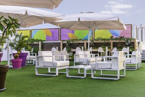 Outdoor seating with white chairs and large umbrellas, surrounded by potted plants and a colorful wall. - Paradise Park Fun Lifestyle Hotel (Arona)