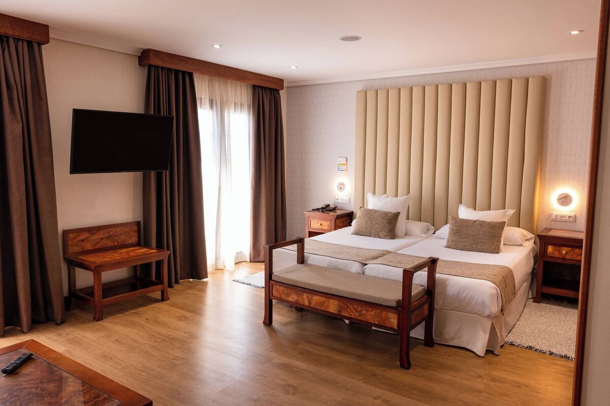 Una habitación de hotel con una cama grande, mesitas de noche, un televisor y un banco.