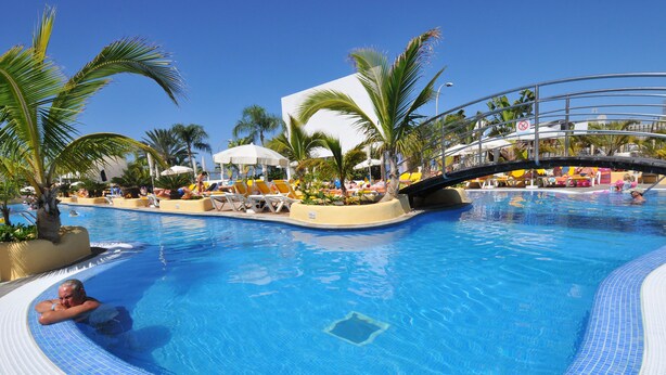A swimming pool with lounge chairs, palm trees, and a bridge. - Paradise Park Fun Lifestyle Hotel (Arona)