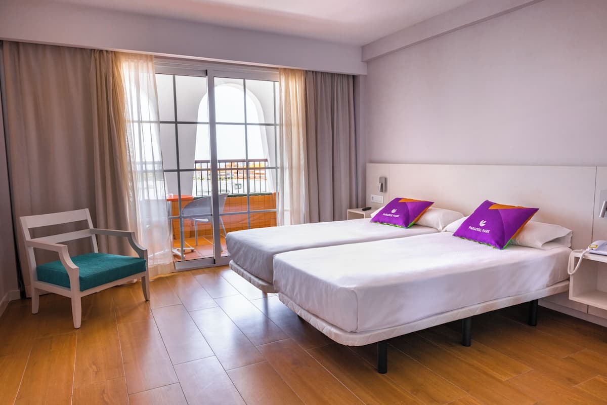 Habitación de hotel con dos camas, una silla y un balcón.