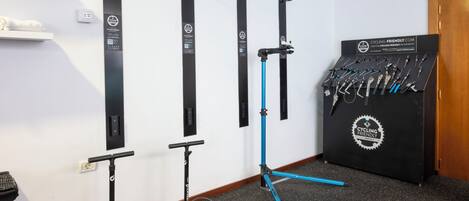 A room with a wall-mounted bike rack, a stand-up bike trainer, and a display of cycling tools.