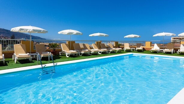 A pool area with lounge chairs and umbrellas, a clear blue sky, and a view of the mountains.