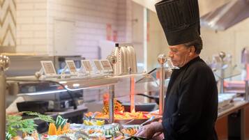 Een buffetgedeelte met diverse soorten eten en iemand die serveert.