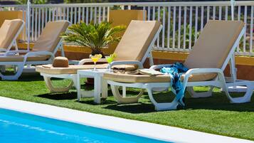 Zona junto a la piscina con sillas de lounge blancas, una mesa pequeña con una bebida y una planta, y vistas a la piscina.