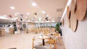 A spacious indoor area with multiple round tables and chairs, a bar area with shelves of bottles, and a large potted plant.