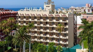A multi-story hotel with balconies, a pool, and a view of the sea.
